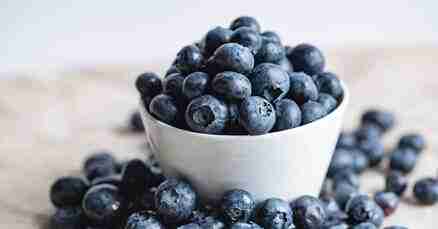 ADHD Essentials: 8 Therapist-Guided Tips for Thriving with Your ADHD Brain 5 A white bowl overflowing with ripe blueberries sits on a wooden surface, like a calming sea of blue amidst the chaos. Additional berries are scattered around the base, each plump and deep in color—perfect for those moments when ADHD essentials include finding peace in simplicity.